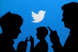 FILE PHOTO: People holding mobile phones are silhouetted against a backdrop projected with the Twitter logo in this illustration picture taken September 27, 2013. REUTERS/Kacper Pempel/Illustration/File Photo