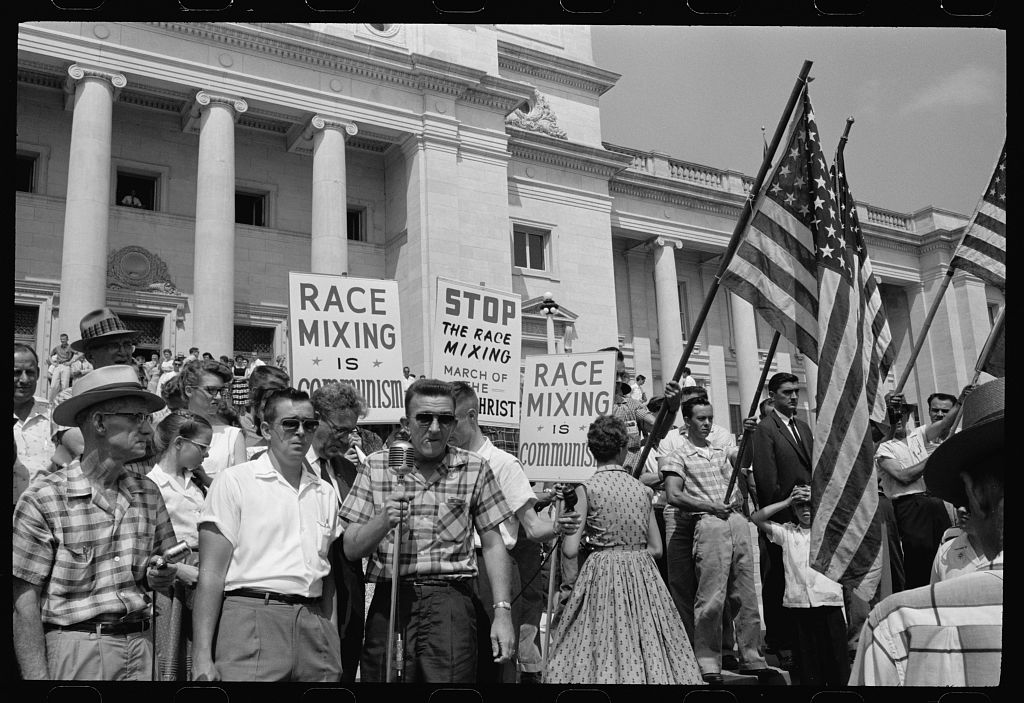 Photograph showing a group of people, several holding signs and American flags, protesting the admission of the "Little Rock Nine" to Central High School ay the Arkansas state capitol in 1959.
