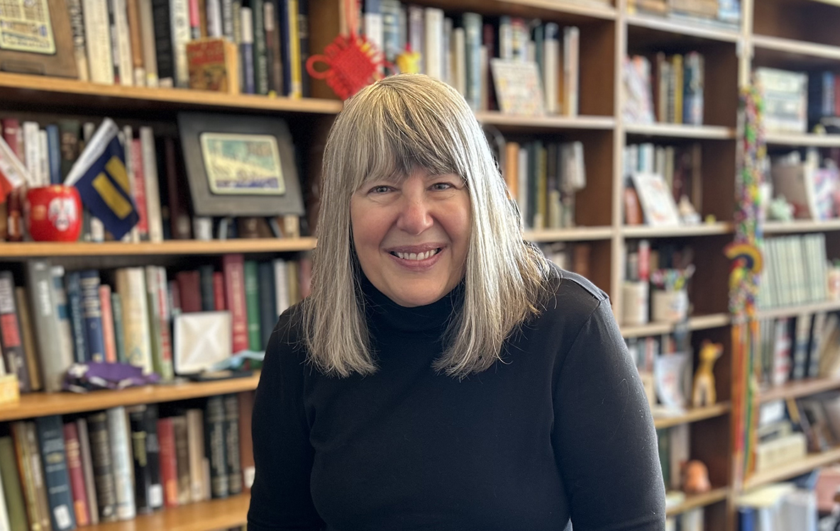 woman with shoulder length hair and black turtleneck in front of bookshelf