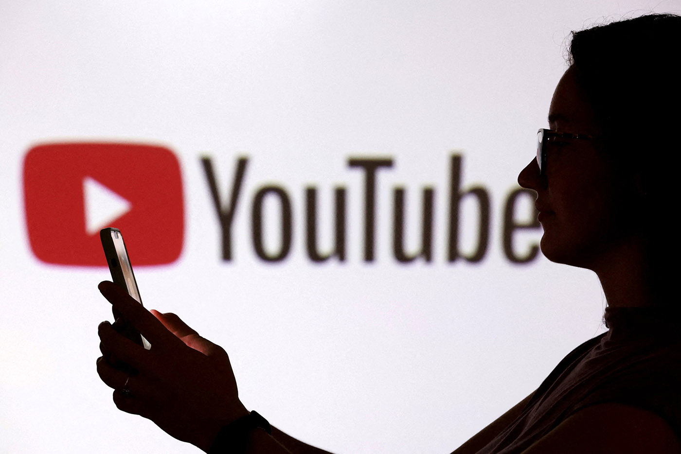 Illustration shows a teenager posing for a photo while holding a smartphone in front of a Youtube logo